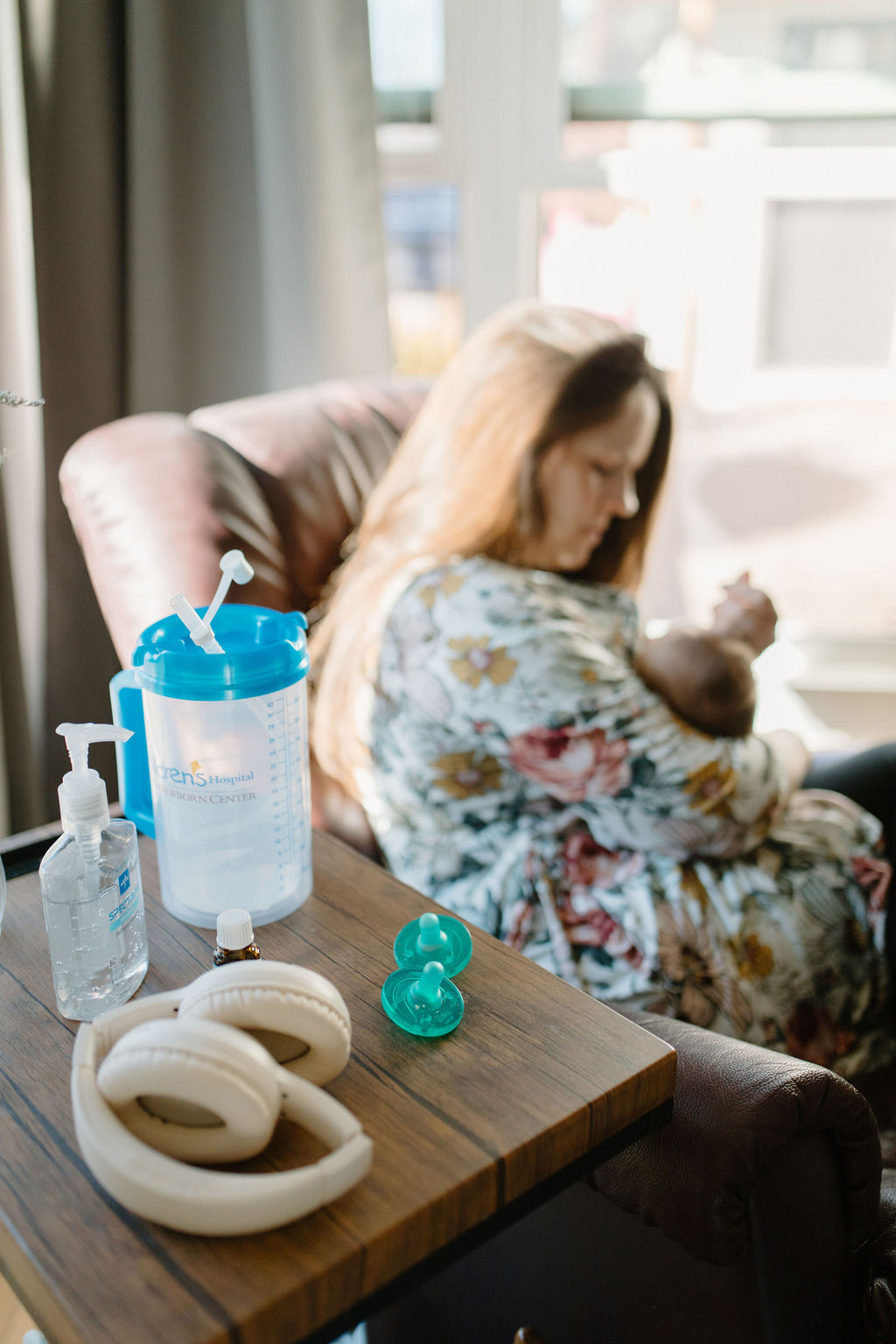 Side table nursing mom on maternity leave shows nursing necessities with mother and child in the background